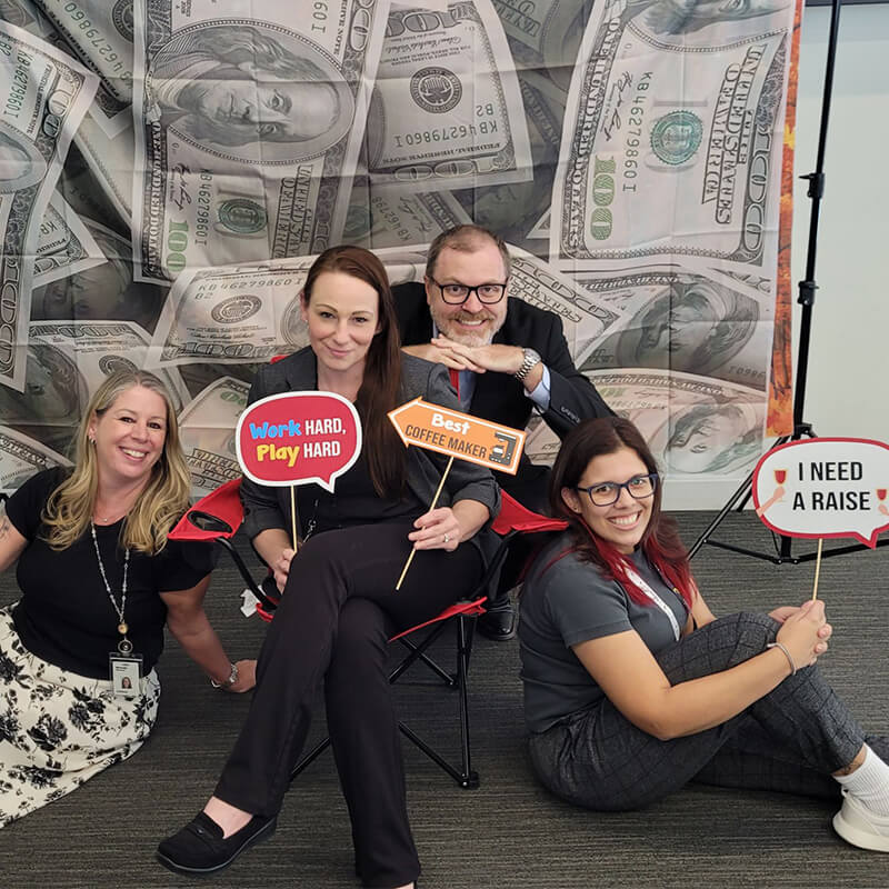 Payroll professionals smiling together holding up props in front of money backdrop.