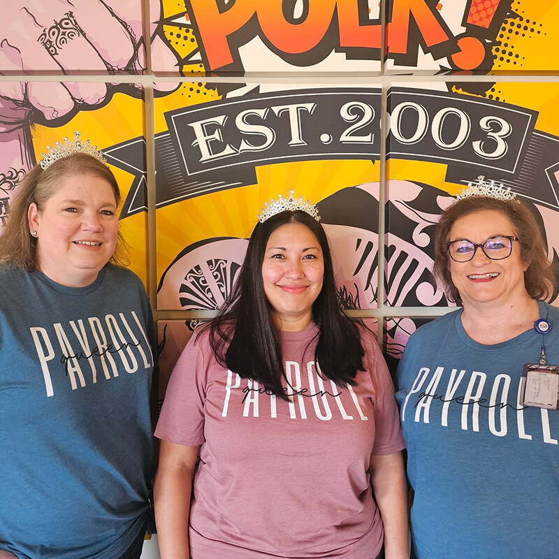 Three women smiling while wearing tiaras.