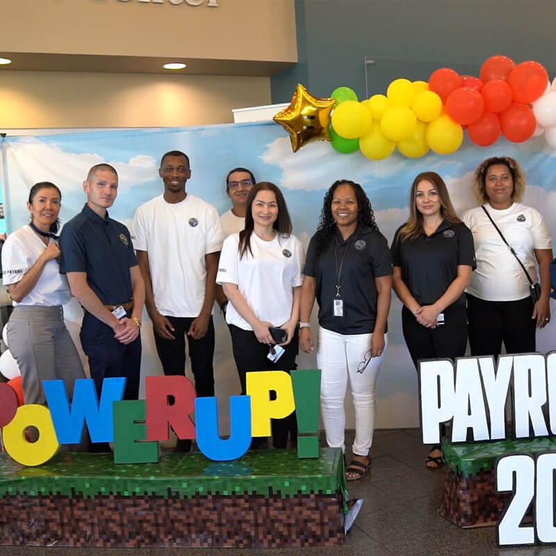 Group of young payroll professionals smiling in front of backdrop of clouds